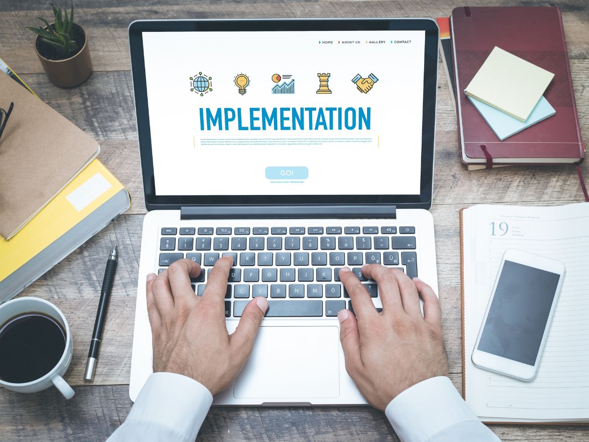 A person typing on a laptop with "Implementation" displayed on the screen.