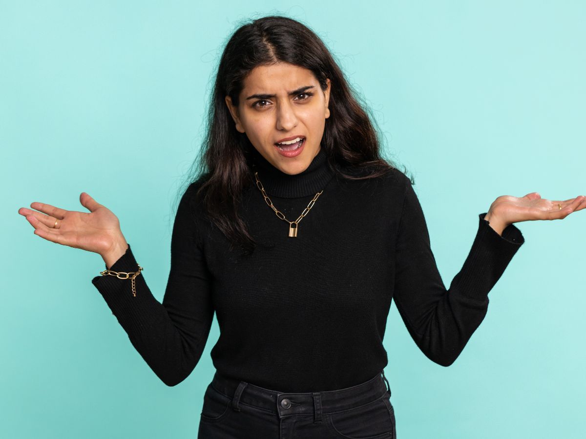A confused woman in black with raised hands, expressing uncertainty or questioning something.